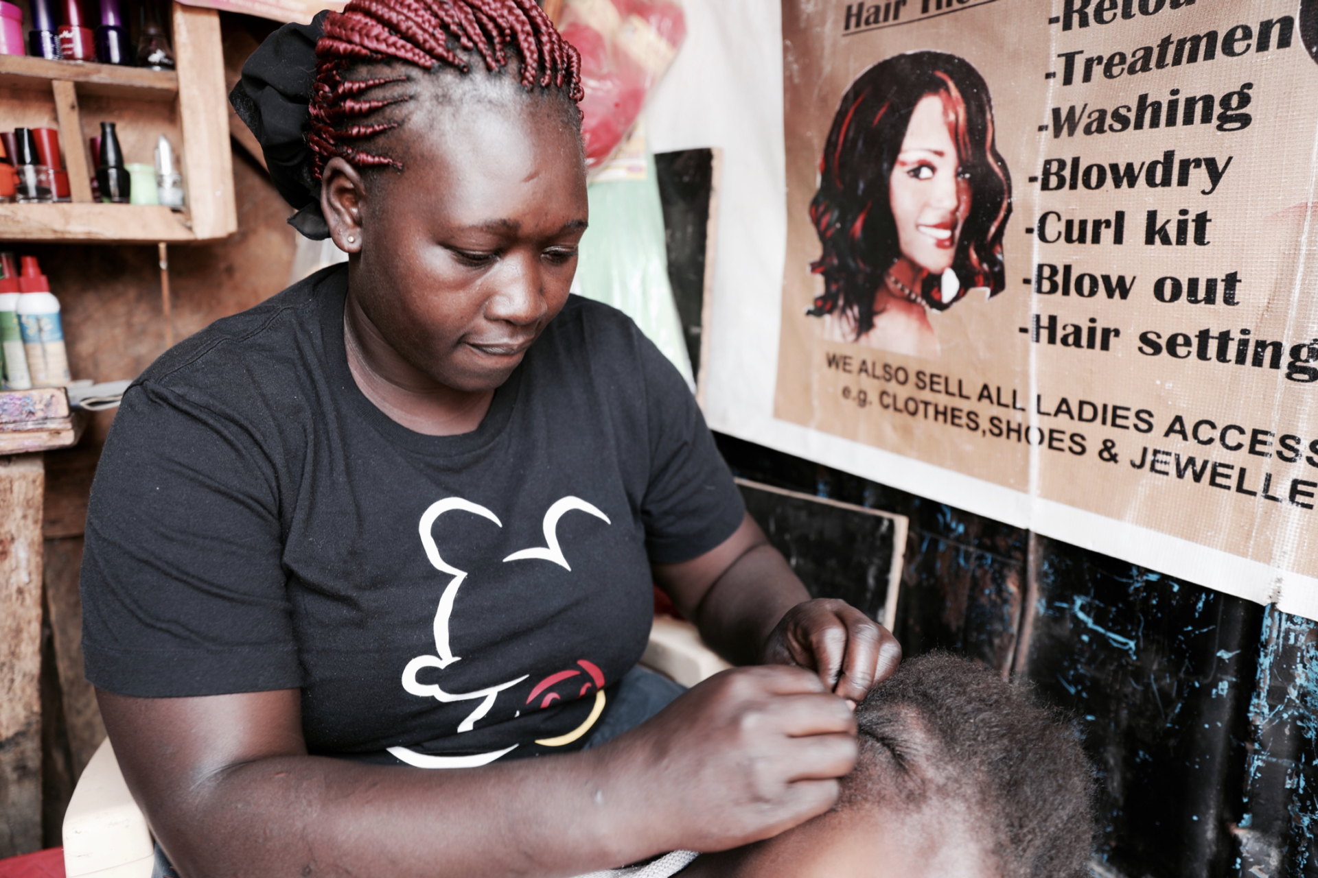 Everlyne, a thirty-five year old mother of three, combs out her daughter’s braids her beauty salon.